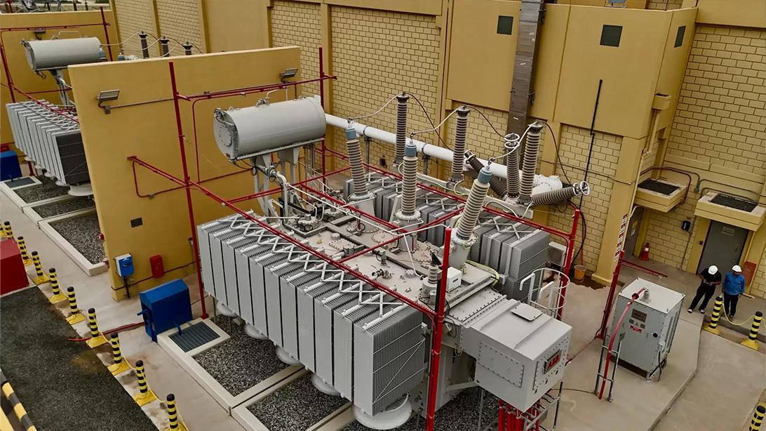 Oil-immersed transformers with conservators and radiators beside an industrial building