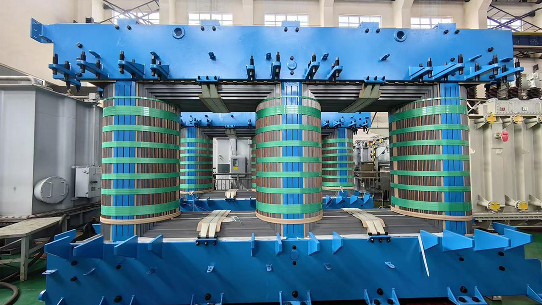 Three transformer winding assemblies supported by blue clamping frames in a workshop
