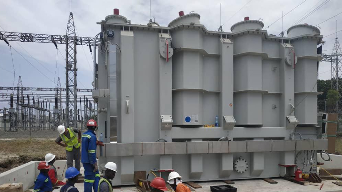 Personnel beside a large transformer tank at an outdoor substation installation